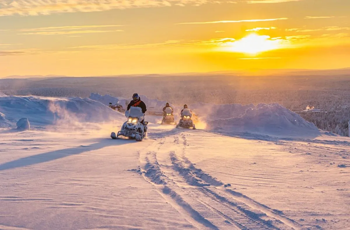 Snowmobile riders crossing a snowy fell at sunset in Finnish Lapland