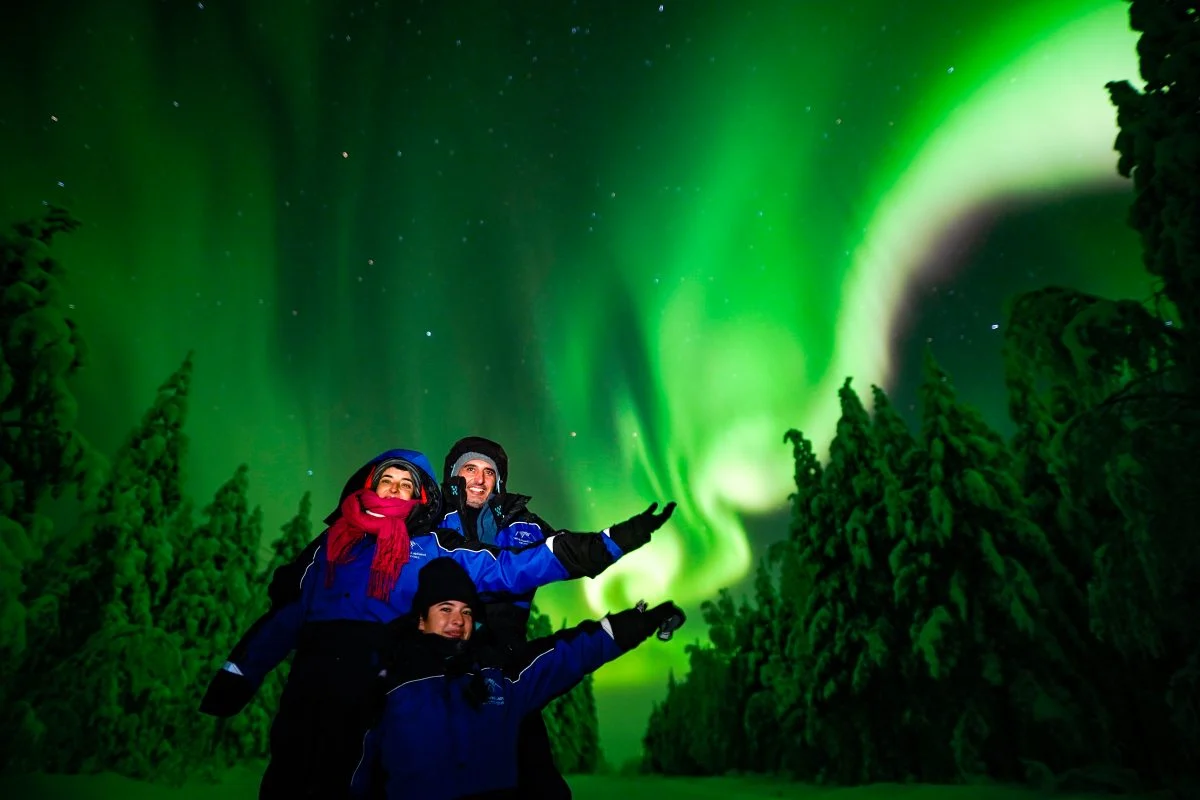 Family in winter overalls beneath the northern lights in Lapland
