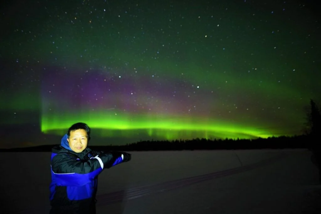 Vieras katselee vihreitä ja violetteja revontulia jäätyneellä järvellä Rovaniemen lähellä