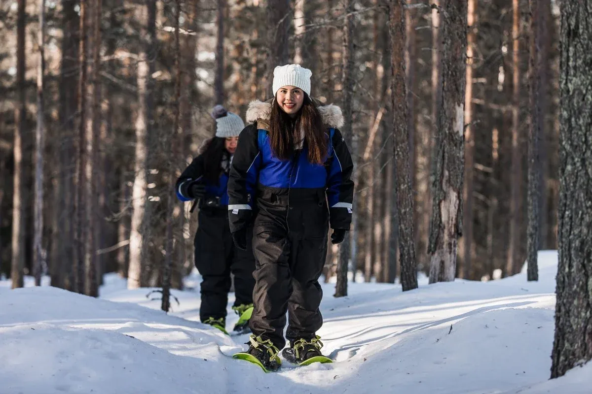 Visitors snowshoeing through a snowy pine forest near Rovaniemi